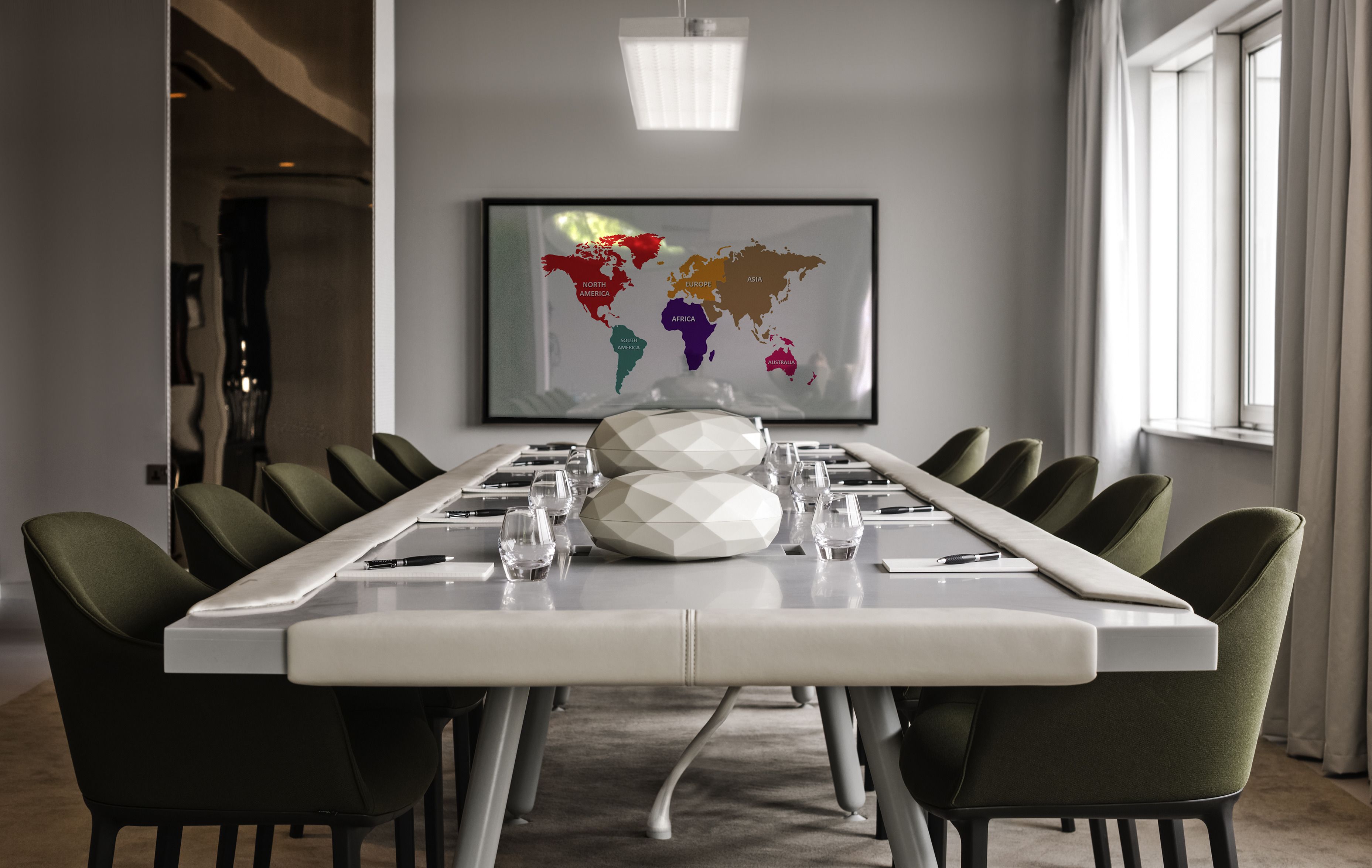 Een vergaderruimte met een lange tafel, groene stoelen en een wereldkaart aan de muur.