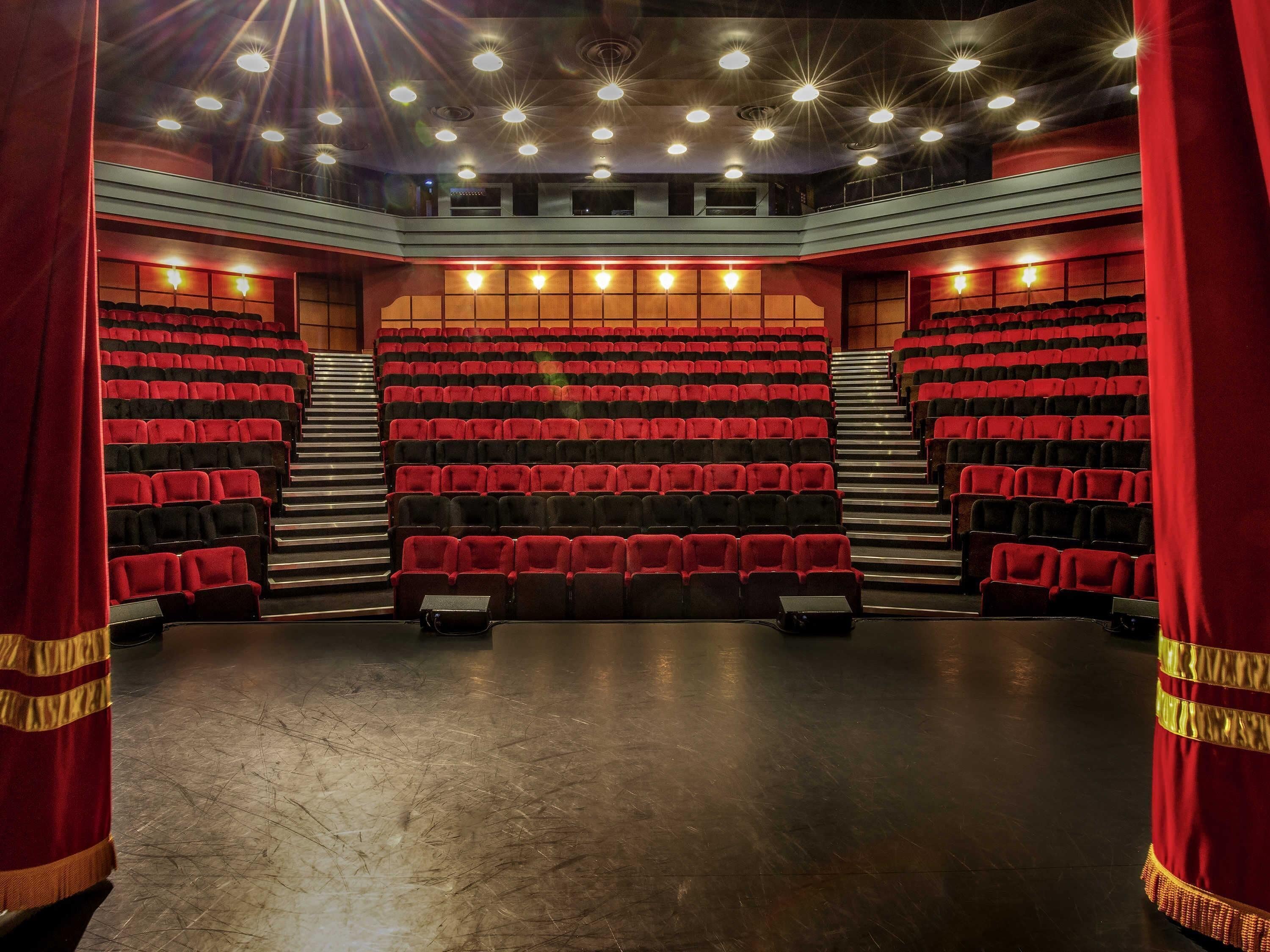 A theater with tiered seating, red curtains, and a stage.