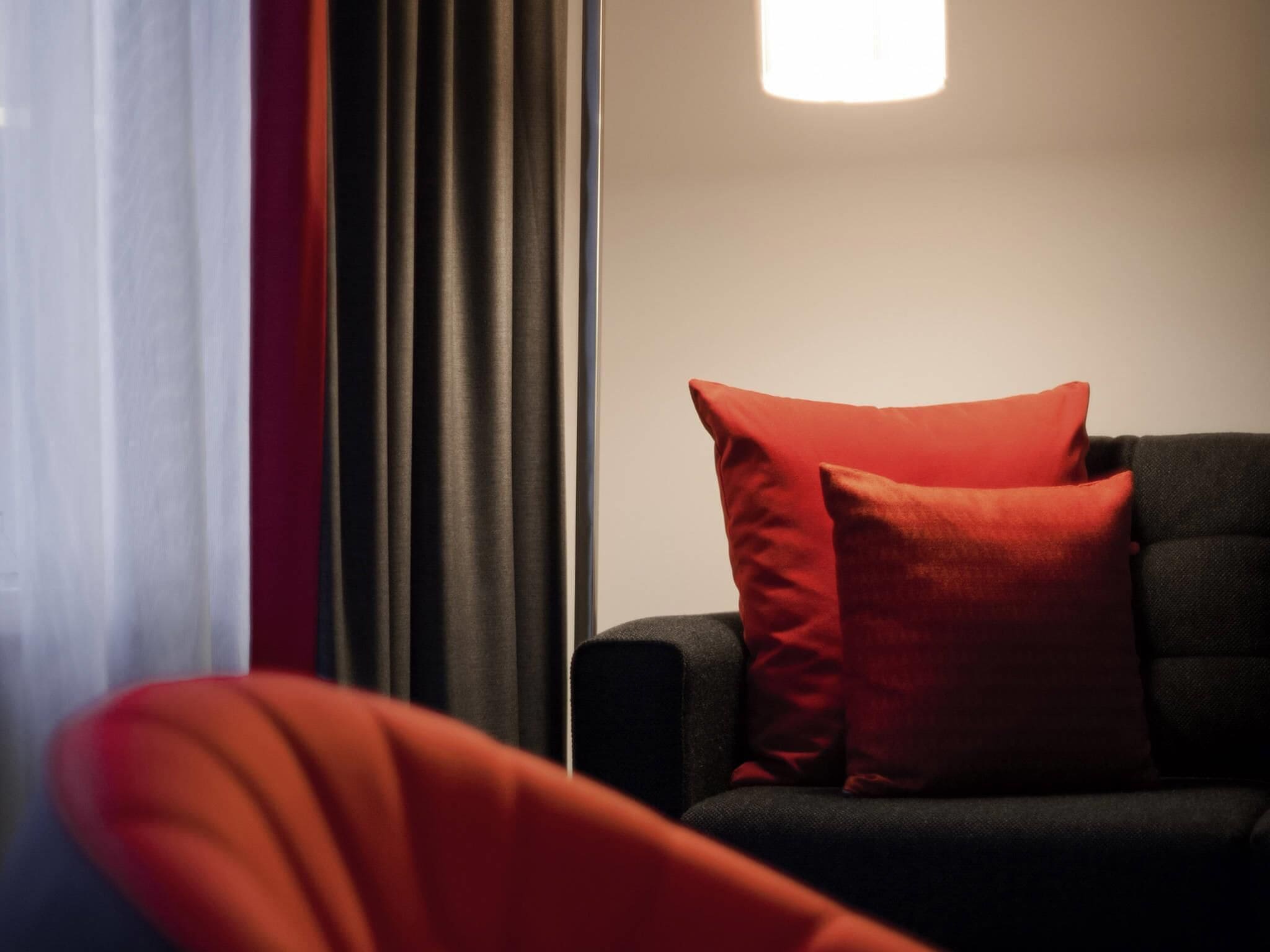 Une pièce moderne avec un canapé foncé et des coussins rouges, un lampadaire et une fenêtre avec des rideaux.