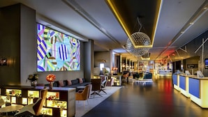 A modern hotel lobby with a large colorful geometric wall art, a reception desk, seating area, and a bar. - Pullman London St Pancras (London)