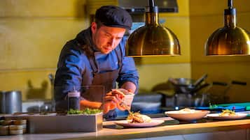 A chef preparing food in a kitchen with yellow walls, stainless steel appliances, and pendant lighting.