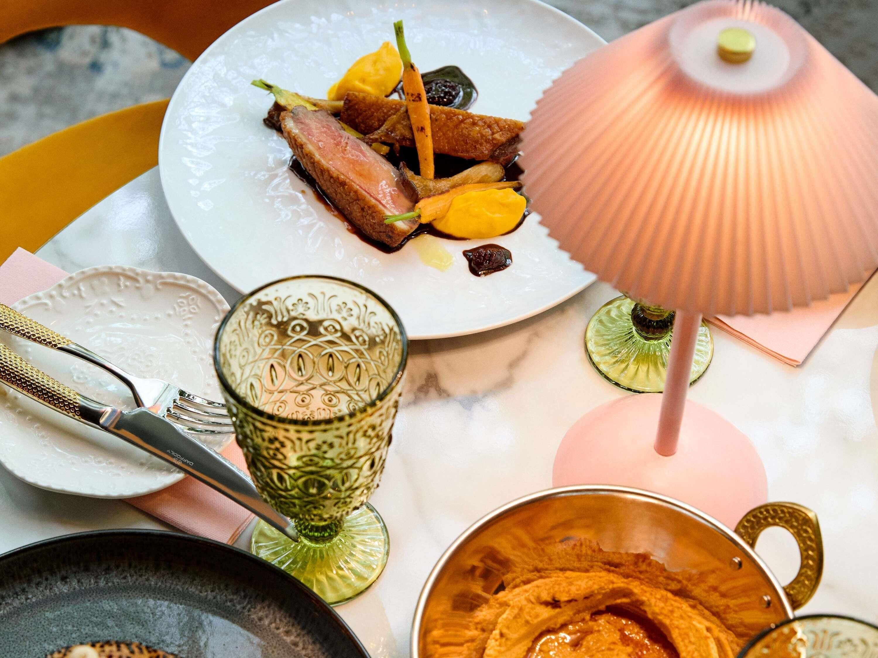 A dining table with a plate of food, a glass, and a decorative lamp.