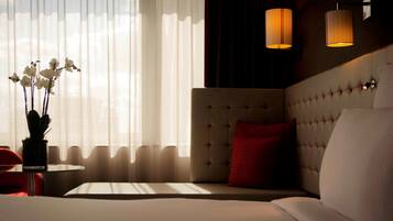 Ein Hotelzimmer mit einem großen Bett, einem roten Sessel, einem kleinen Tisch und einer Vase mit weißen Blumen.