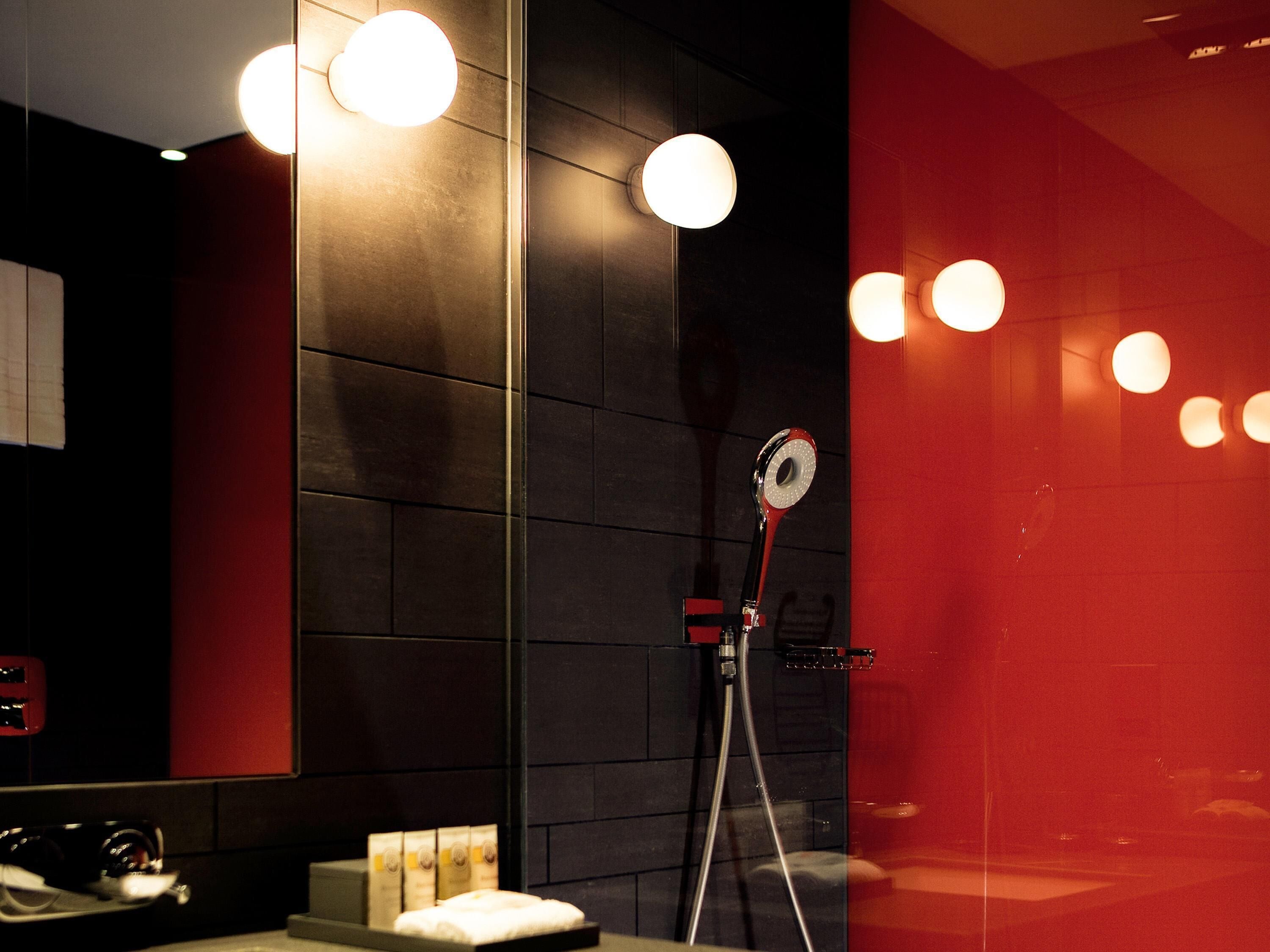A modern bathroom with a large mirror, a handheld showerhead, and a towel rack.