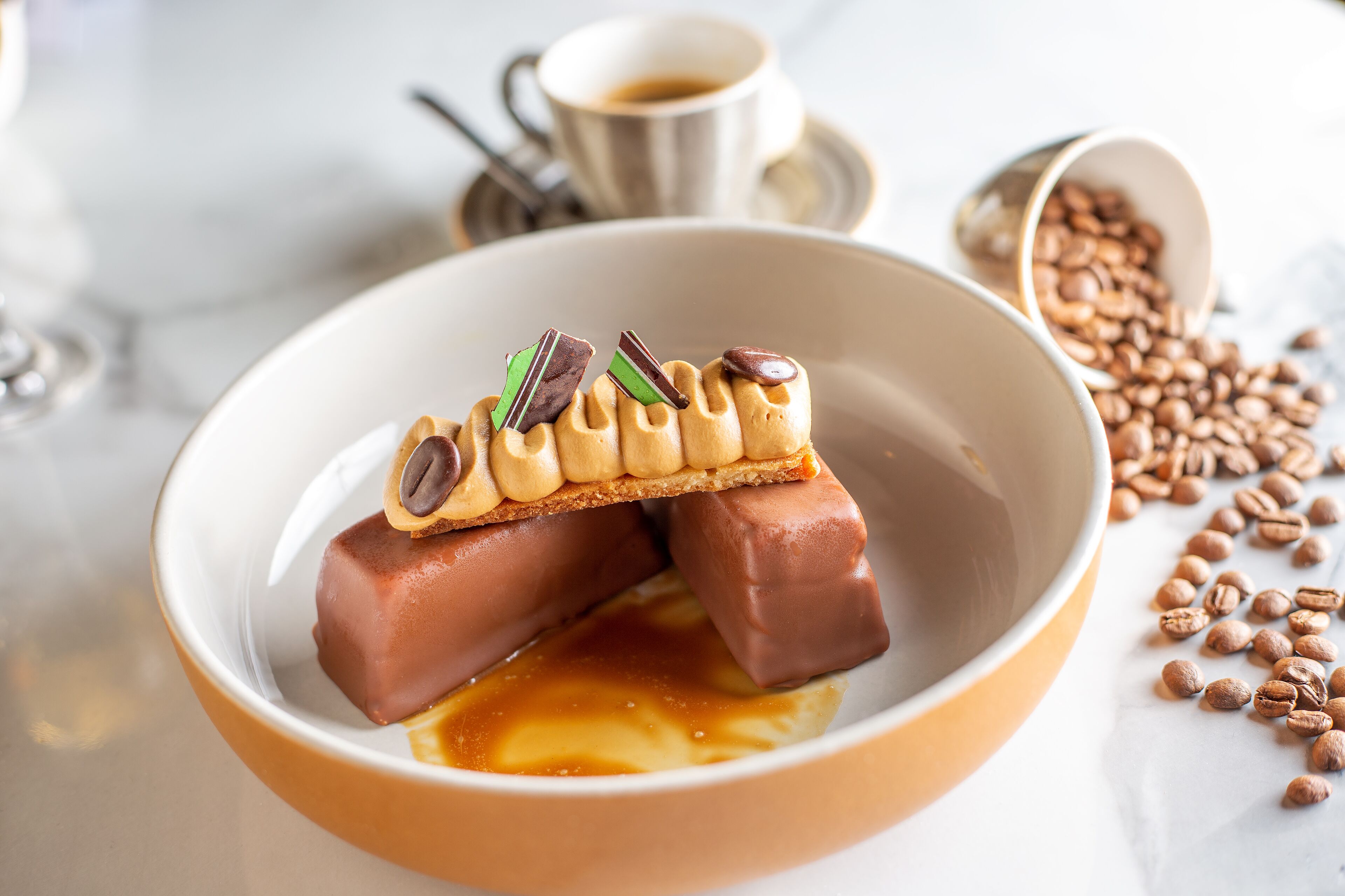 A dessert with caramel and chocolate elements, a cup of coffee, and scattered coffee beans.