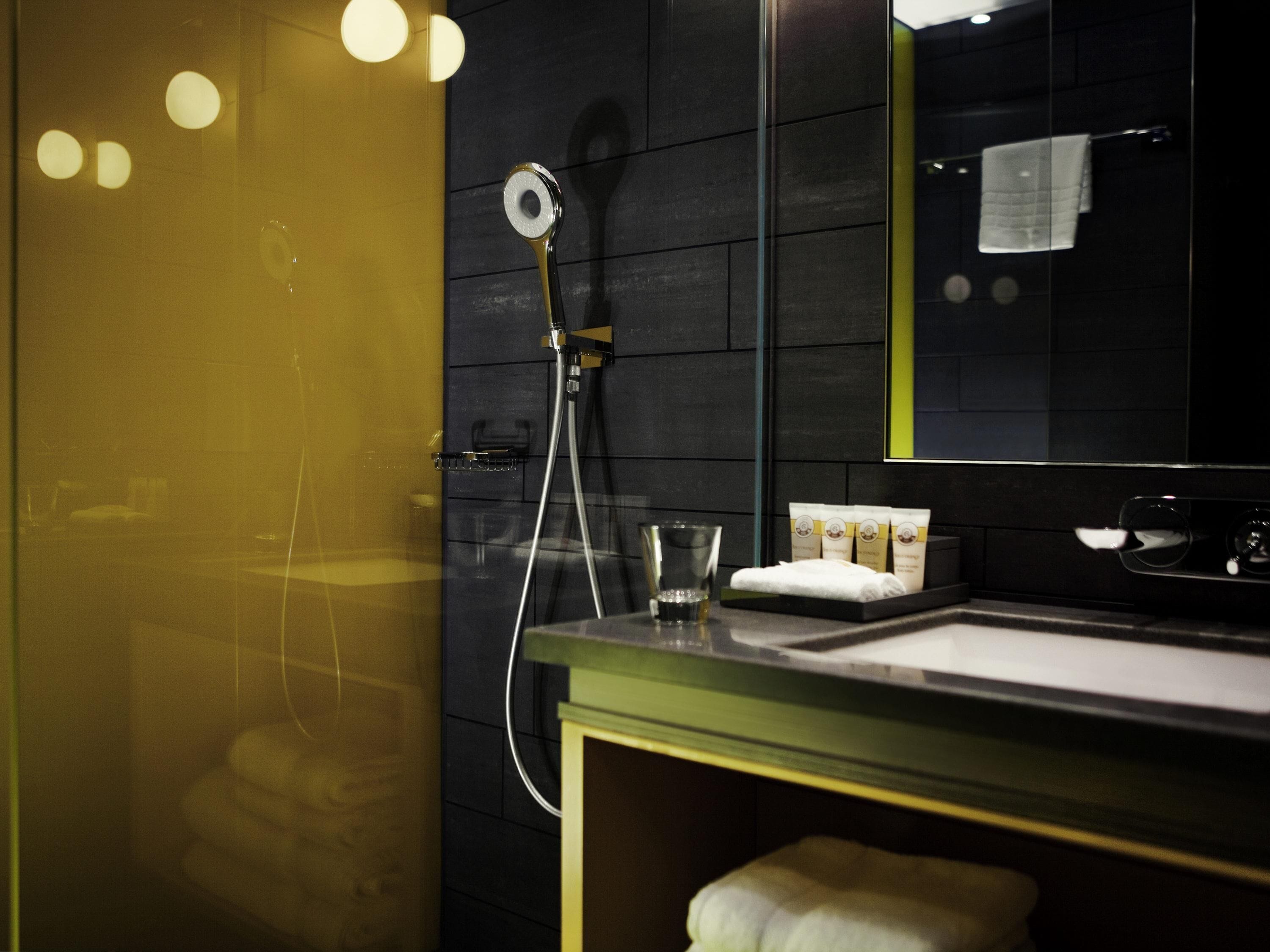 Une salle de bain moderne avec une douche, un verre d’eau et des articles de toilette posés sur le comptoir.