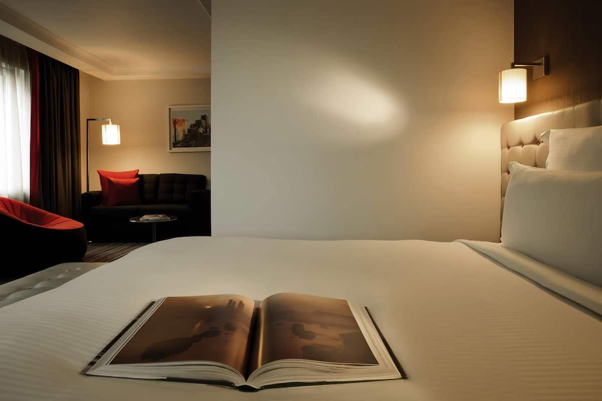 A hotel room with a large bed, a reading chair, a small table, and a nightstand.