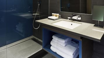 Un baño moderno con ducha de vidrio, lavamanos con espejo y repisa con toallas dobladas.