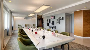 Un salón de conferencias con una larga mesa, sillas verdes y una lámpara de techo moderna.