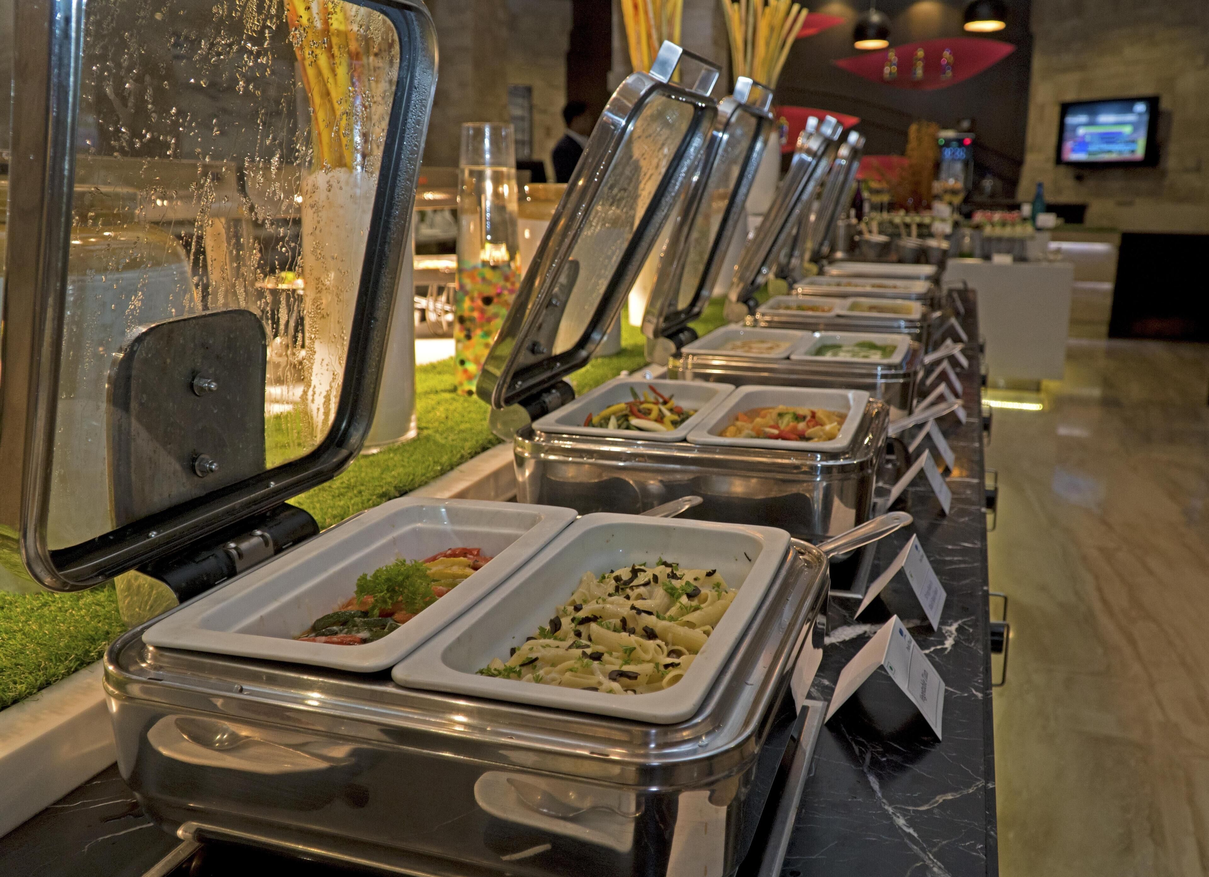 A buffet line with multiple food stations, each with a clear serving tray.