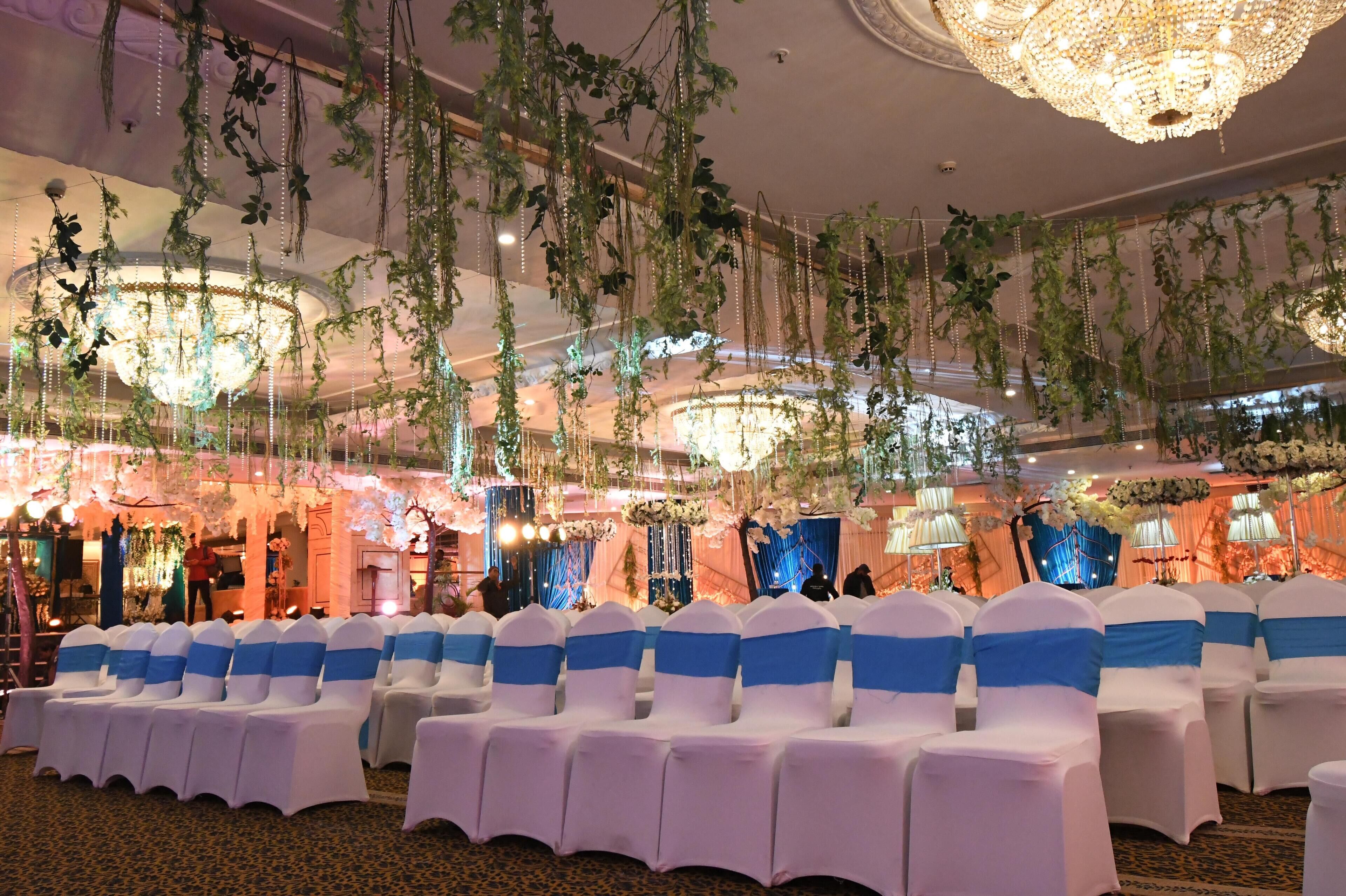 A banquet hall with rows of white chairs with blue sashes, a chandelier, and hanging greenery.