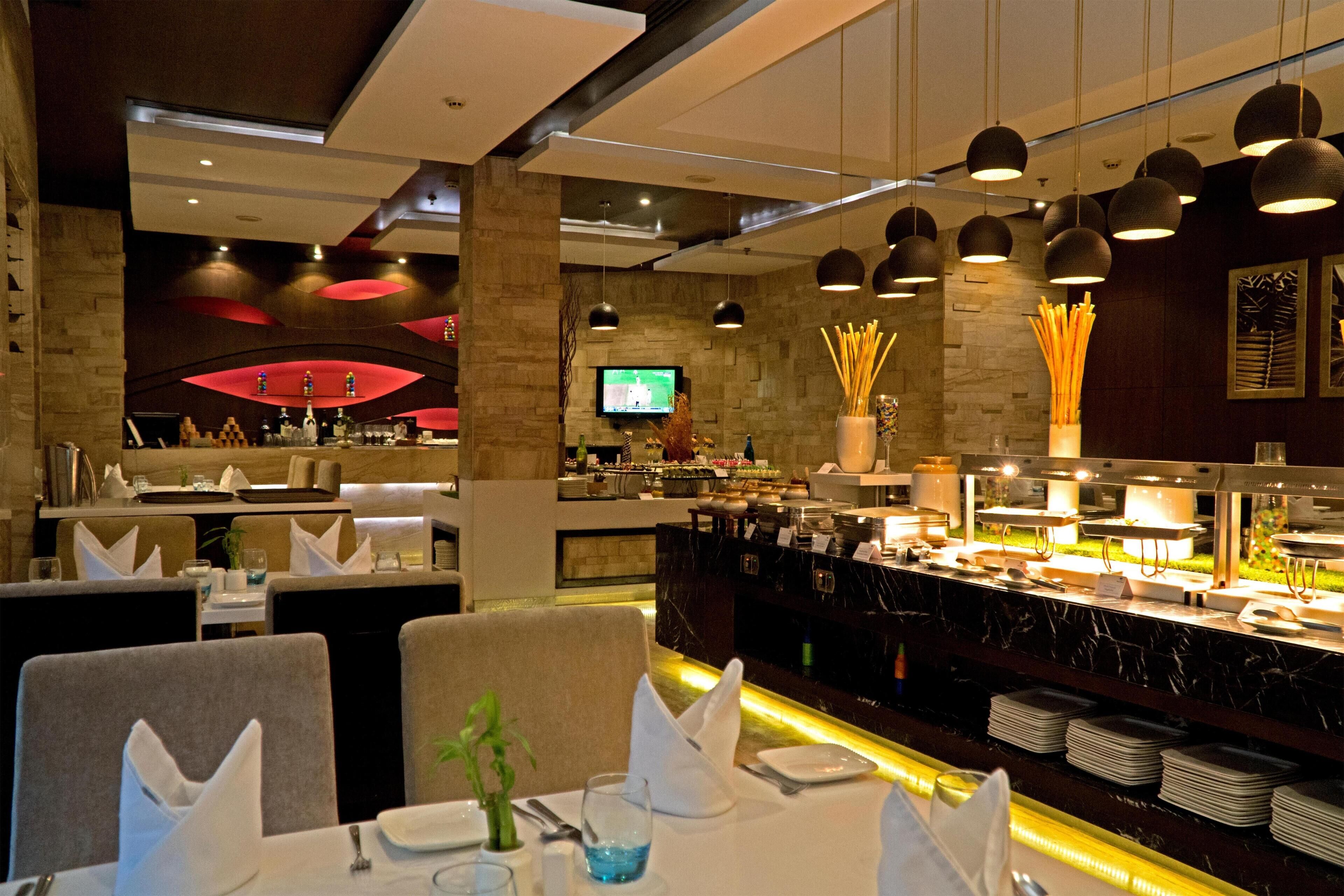 A restaurant with a buffet setup, a television screen, and a bar area.
