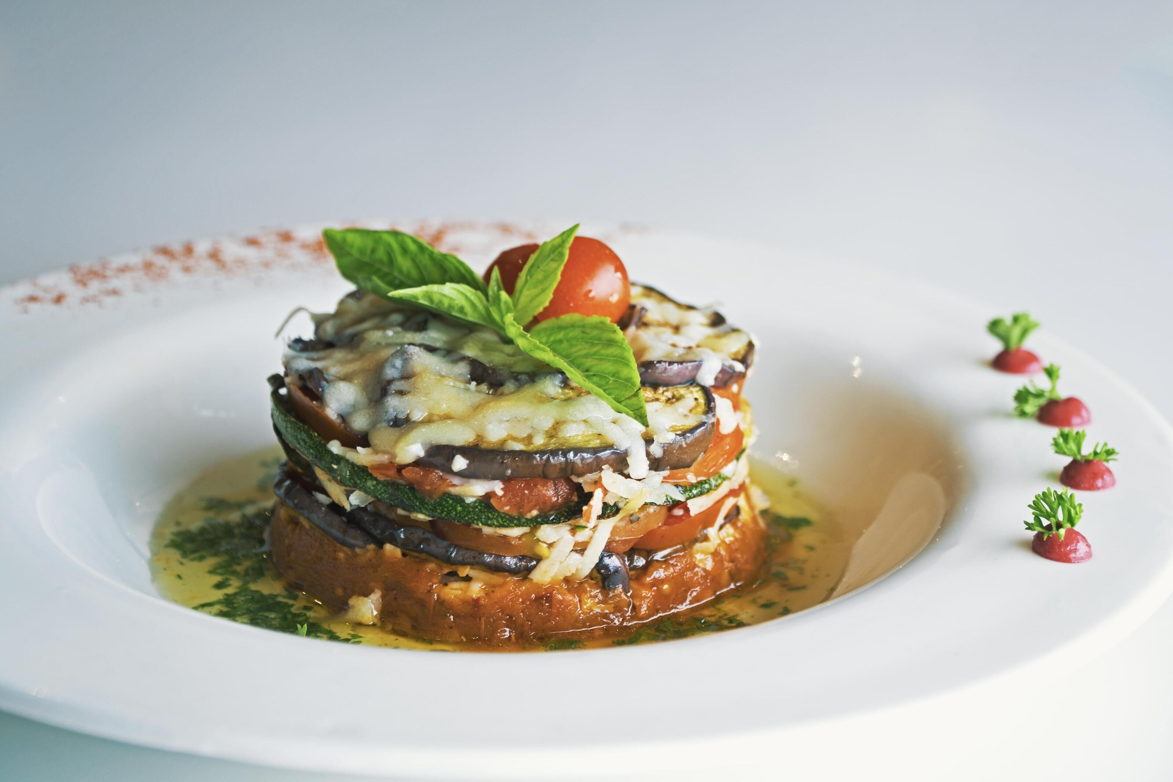 Un plat composé de légumes et de fromage disposés en couches, servi dans une assiette blanche.