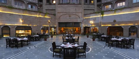 Un amplio patio con varias mesas y sillas para comer, rodeado por un edificio de gran altura con balcones.