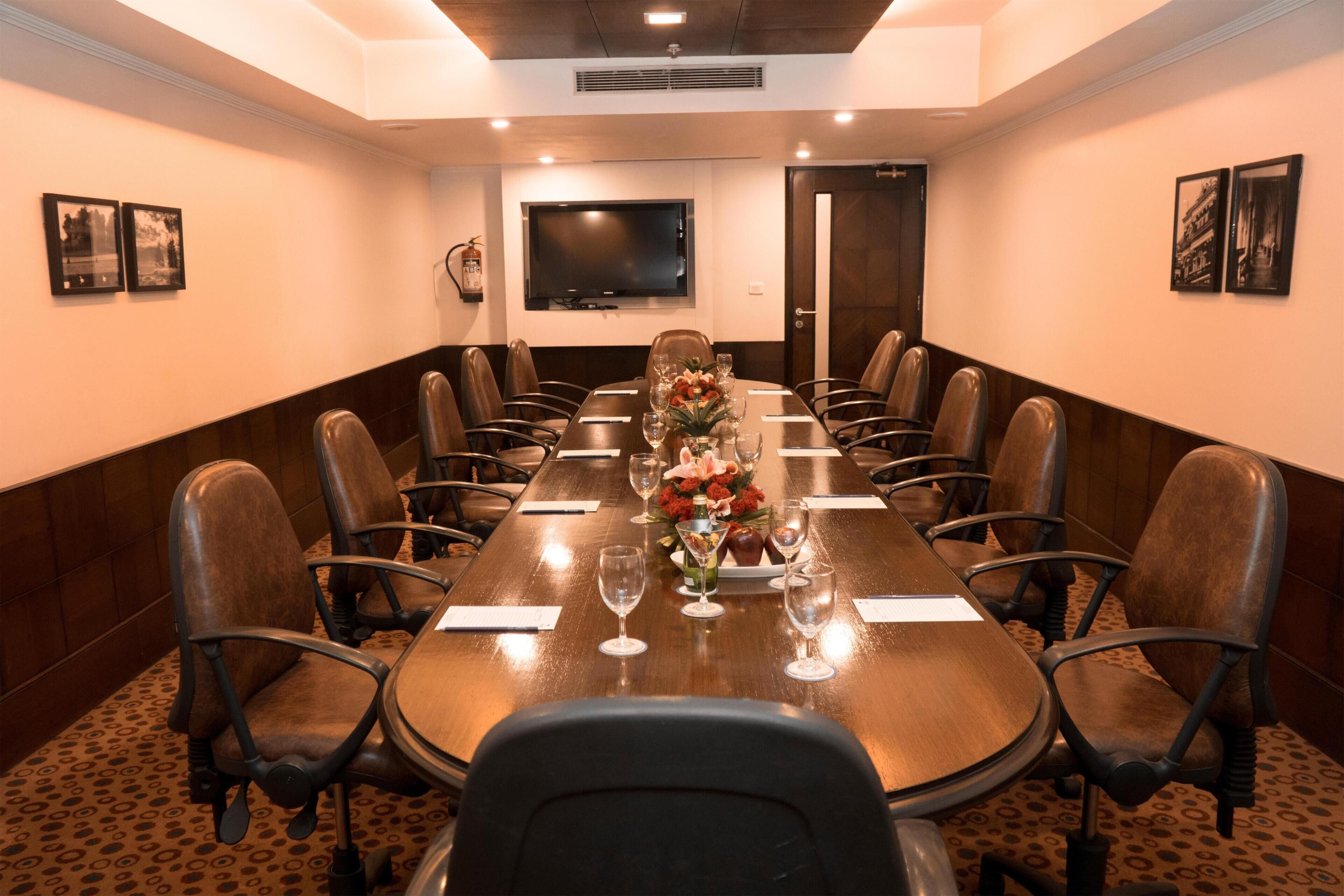 A conference room with a long table, chairs, a television, and framed pictures on the walls.