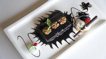 Un plato de postre con un cuadrado cubierto de chocolate, una bola de helado con cereza y un pequeño remolino verde.