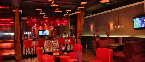 A bar area with red seating, a bar counter, and overhead lighting.