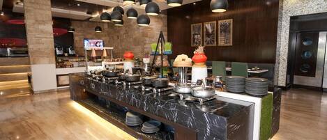 A modern hotel lobby with a marble reception desk, black pendant lighting, and a television screen.