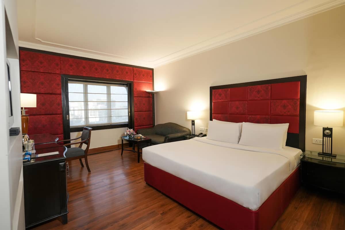 A hotel room with a large bed, a desk, a chair, a window, and two bedside lamps.