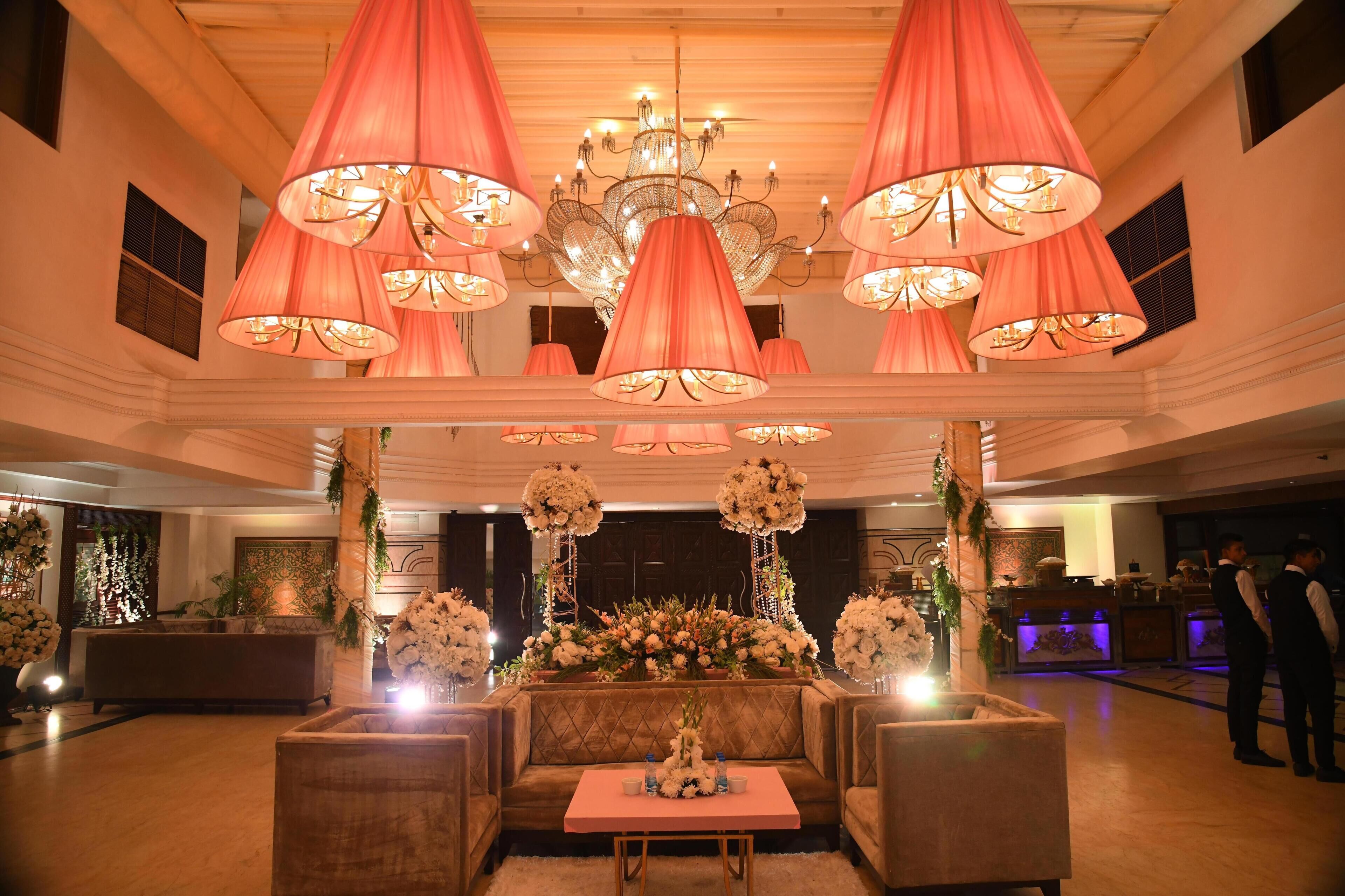 A spacious lobby with a central seating area, multiple chandeliers, and floral arrangements.