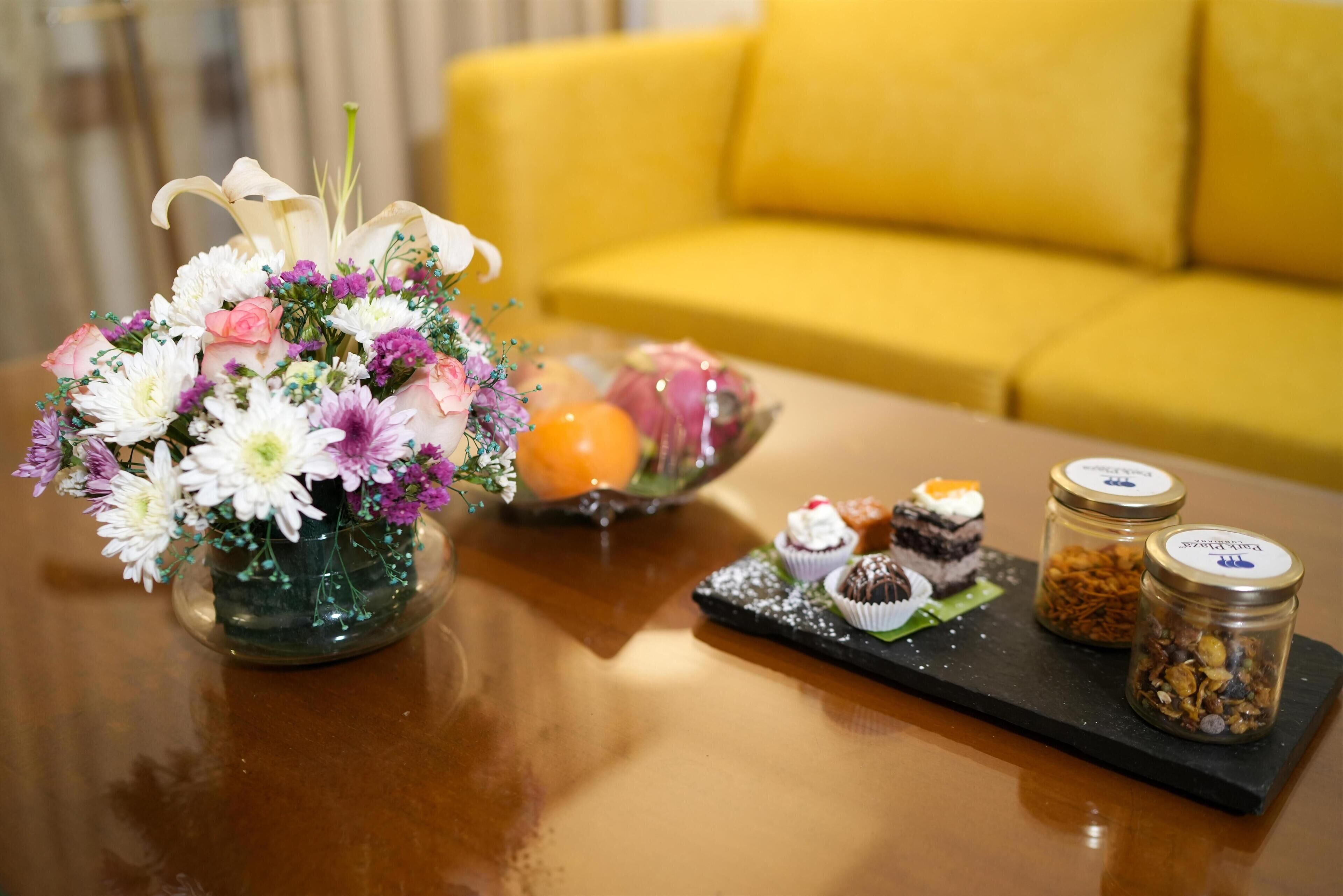 A table with a floral arrangement, a tray with desserts, and two jars of nuts.