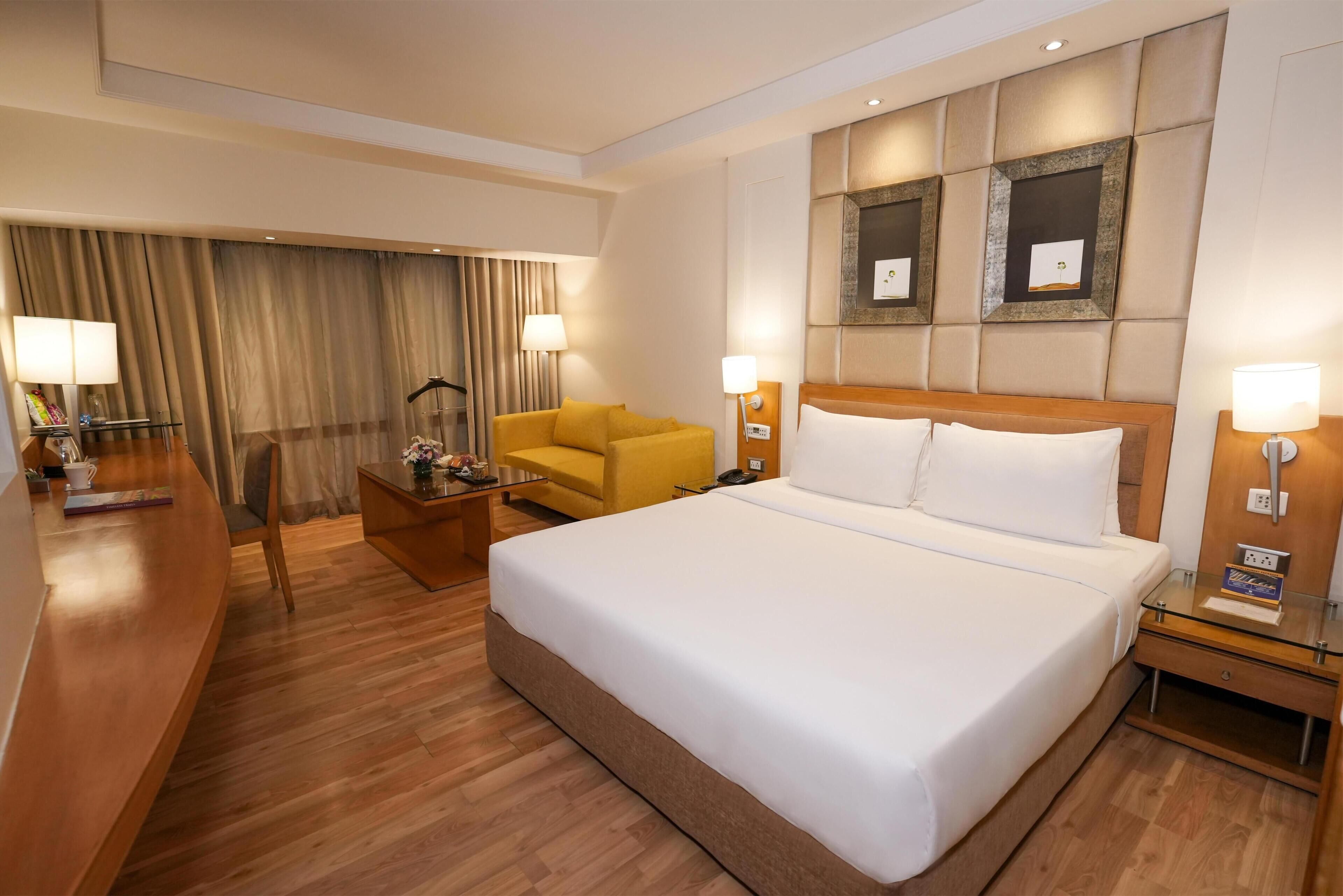 A hotel room with a large bed, a desk, a chair, and a sofa.