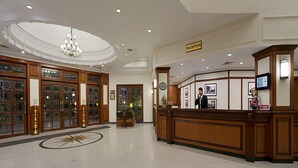 A spacious lobby with a reception desk, a chandelier, and a large decorative mirror.