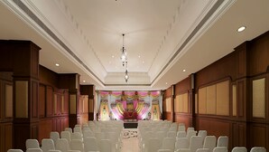 A conference room with rows of white chairs, a stage with colorful drapery, and chandeliers.