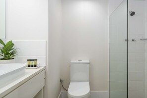 Une salle de bain avec des toilettes blanches, une douche en verre, un lavabo avec un miroir et une plante en pot.