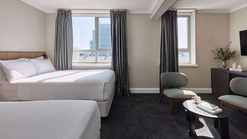A hotel room with two beds, a desk, a chair, and a view of the city.