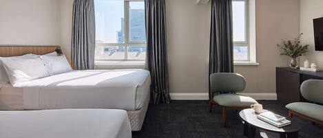 Habitación de hotel con dos camas, un escritorio, una silla y vistas a la ciudad.