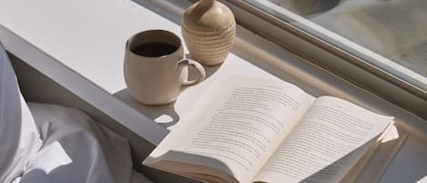 Un llit amb un llibre i una tassa a la finestra.