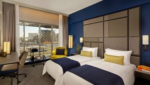 A hotel room with two beds, a desk, a chair, and a view of the cityscape. - Park Plaza Utrecht (Utrecht)