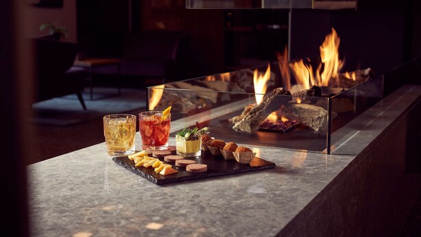 A bar area with a glass-top table featuring a drink, snacks, and a fireplace. - Park Plaza Utrecht (Utrecht)