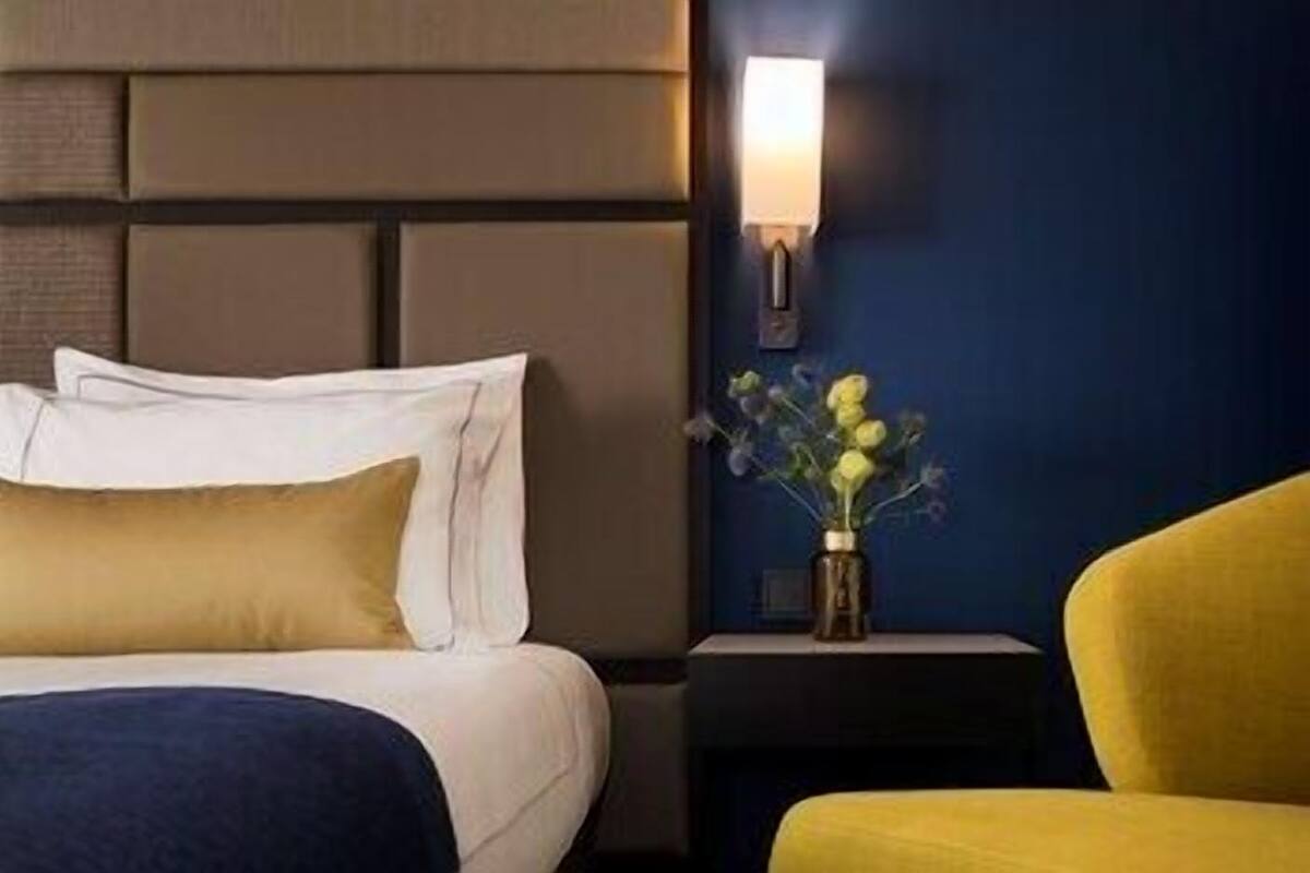 A hotel room with a bed, a nightstand with a vase of flowers, and a yellow armchair.