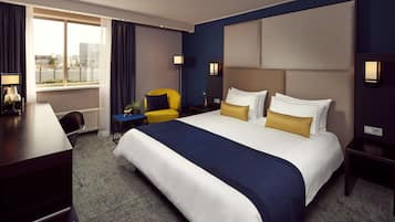 Una habitación de hotel con una cama grande, un escritorio, una silla y un ventanal con cortinas.