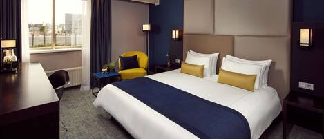 A hotel room with a large bed, a desk, a chair, and a window with curtains.