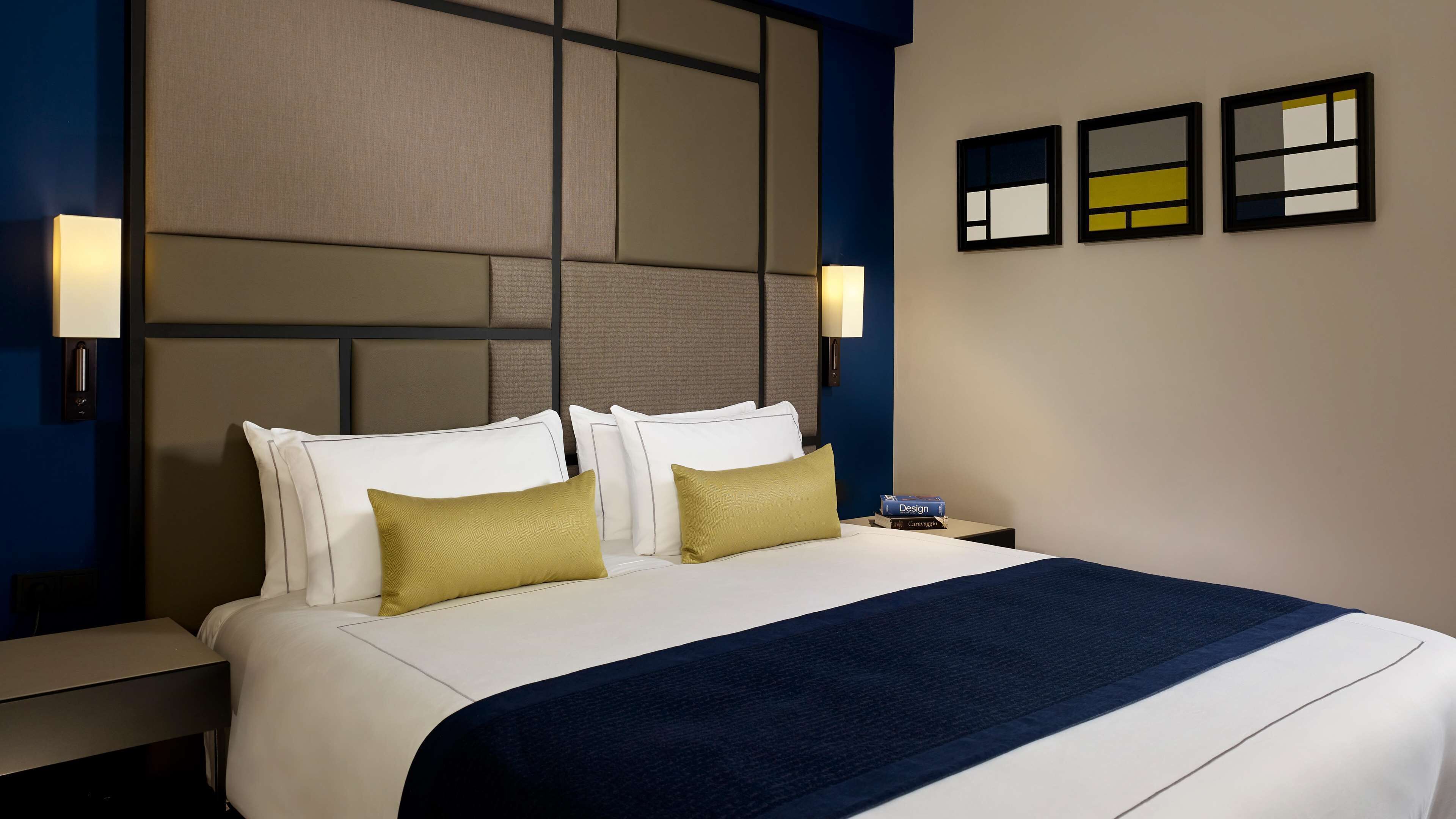 A hotel room with a large bed, two bedside tables, a nightstand, and a wall-mounted lamp.