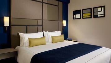 A hotel room with a large bed, two bedside tables, a nightstand, and a wall-mounted lamp.