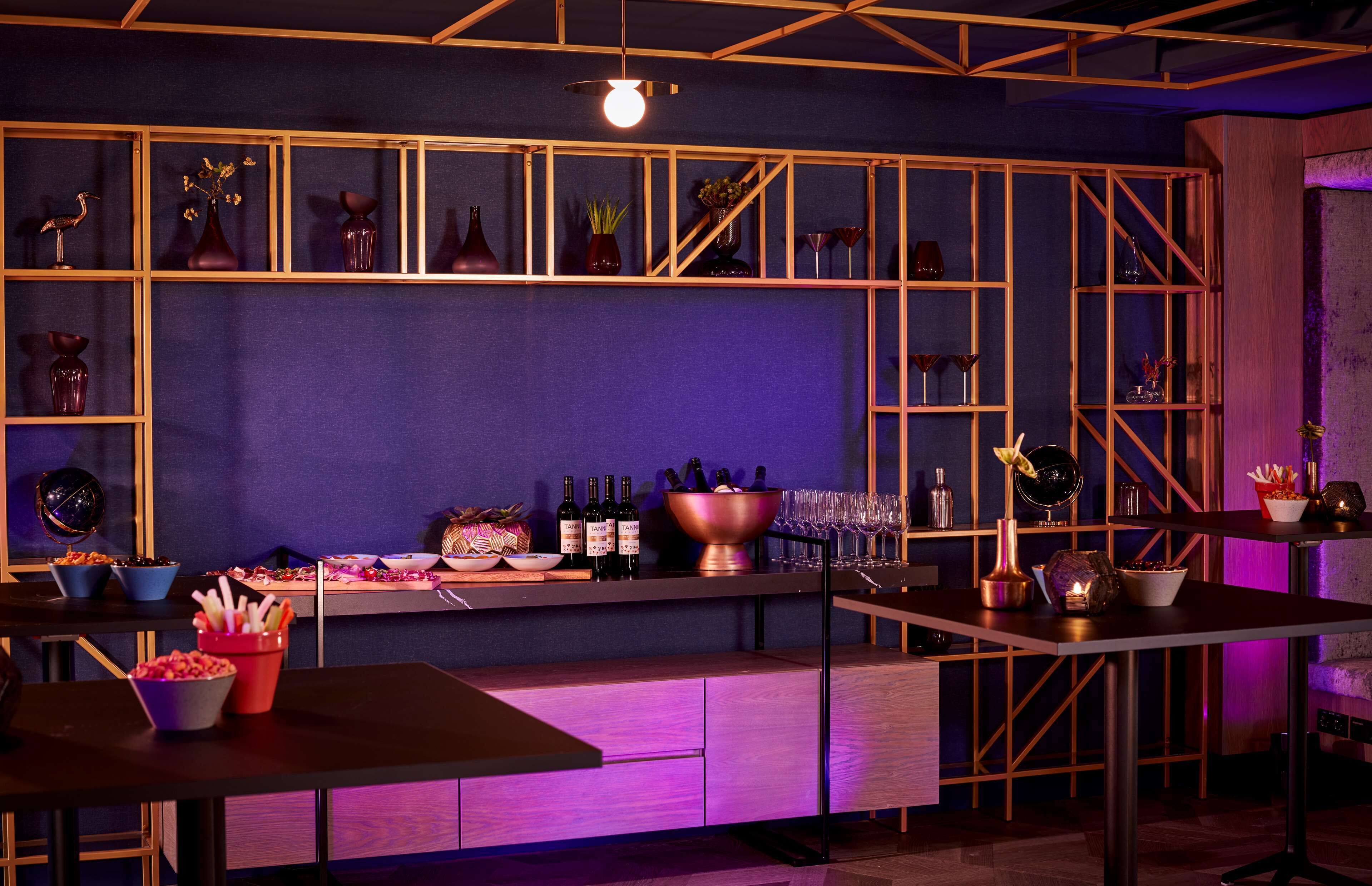 Una zona de bar con estantes llenos de botellas y vasos, un frutero y una mesa con una vela.