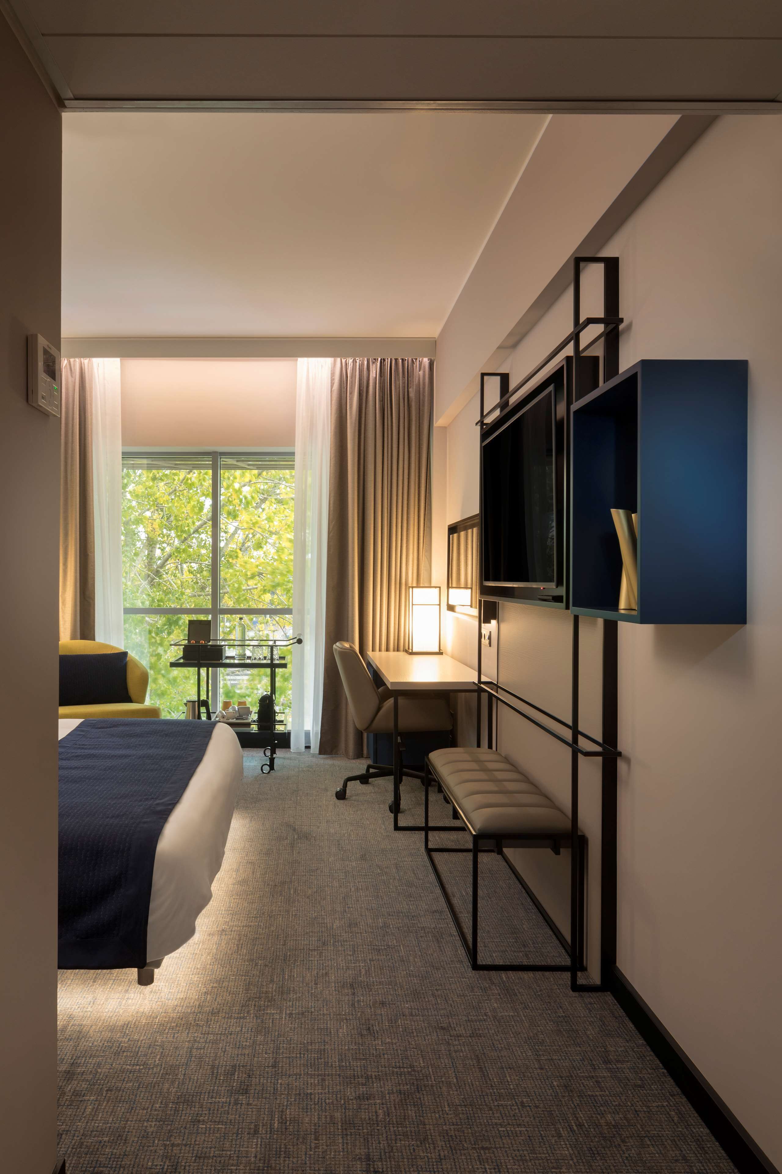 A hotel room with a bed, desk, chair, and TV.