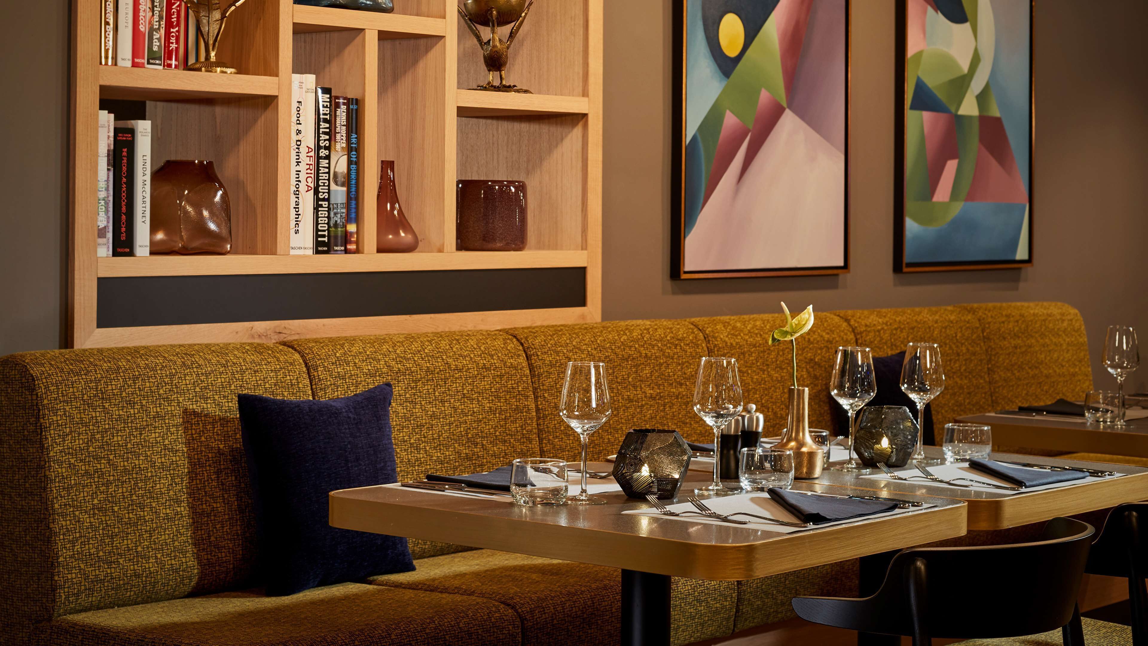 A restaurant with a wooden bookshelf, a brown sofa, and a table set with wine glasses and cutlery.