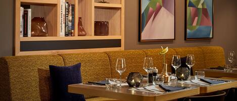 A restaurant with a wooden bookshelf, a brown sofa, and a table set with wine glasses and cutlery.