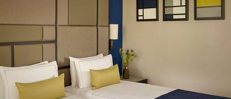 A hotel room with a large bed, two bedside tables, a nightstand, a lamp, and three framed artworks on the wall.