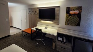 Una camera d'albergo con scrivania, sedia, televisore e un quadro di un cactus appeso al muro.