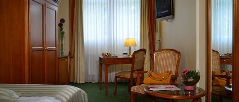 Habitación de hotel con cama, escritorio con lámpara, dos sillas, televisor y maleta.