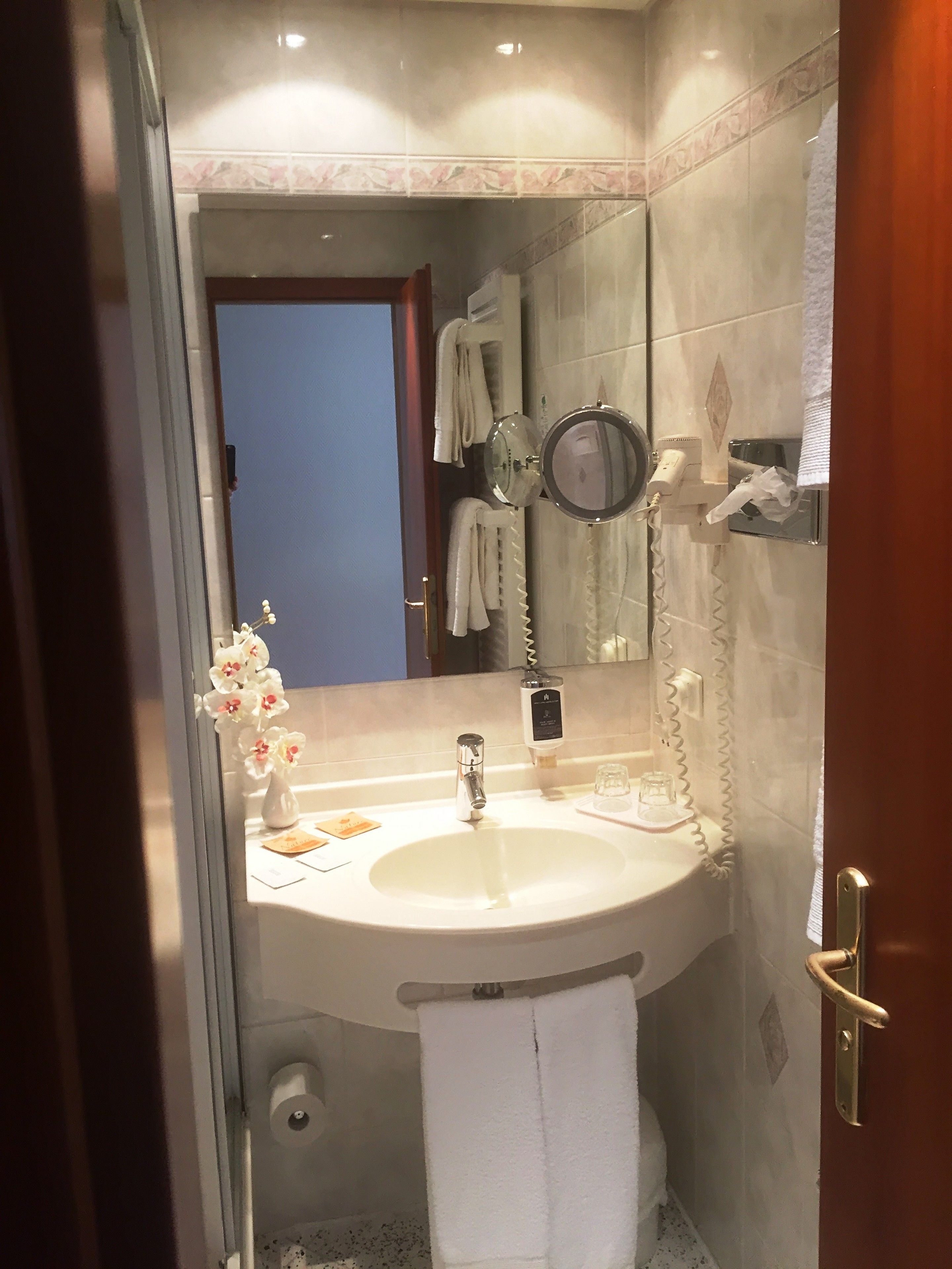 A bathroom with a sink, mirror, towel rack, and a small vase with flowers.