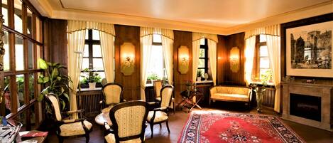 A traditional room with wooden paneling, a red patterned rug, and multiple seating areas with upholstered chairs.