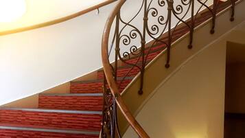 A spiral staircase with a wooden handrail and metal balusters, leading to a landing with a wall-mounted light fixture.