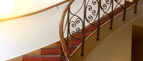 A spiral staircase with a wooden handrail and metal balusters, leading to a landing with a wall-mounted light fixture.